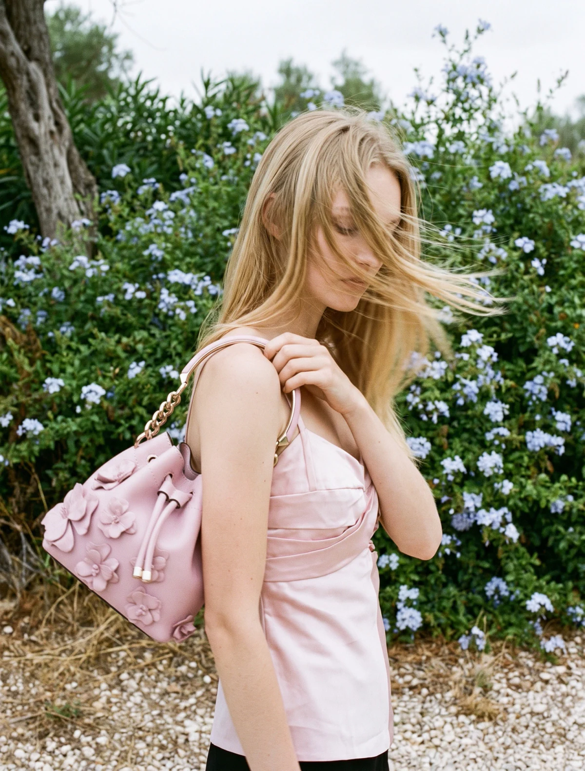 AI-generated on-model image: pink shoulder bag and cotton top photographed against flowering shrubs