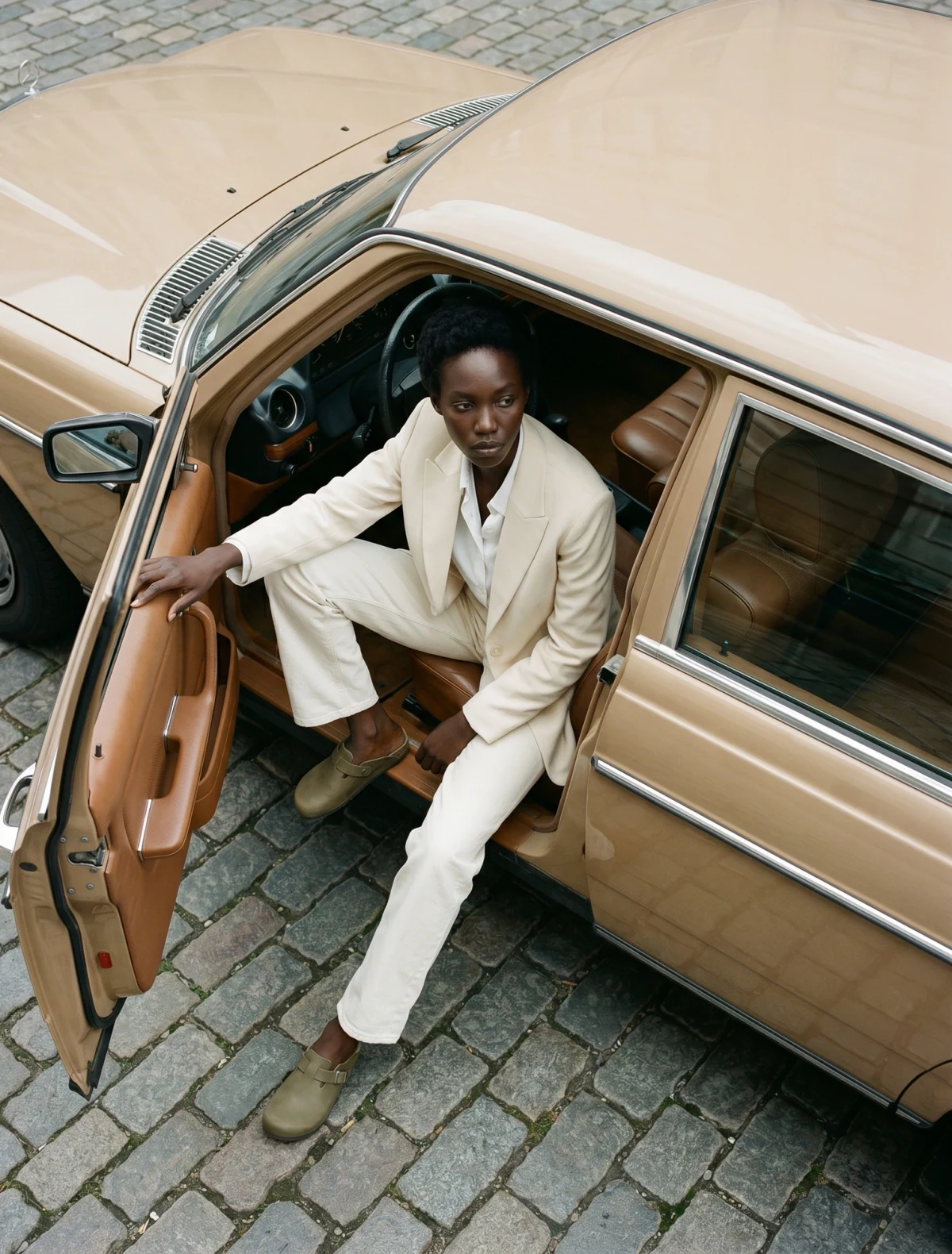 AI-generated on-model image: cream tailoring photographed stepping out of a vintage car