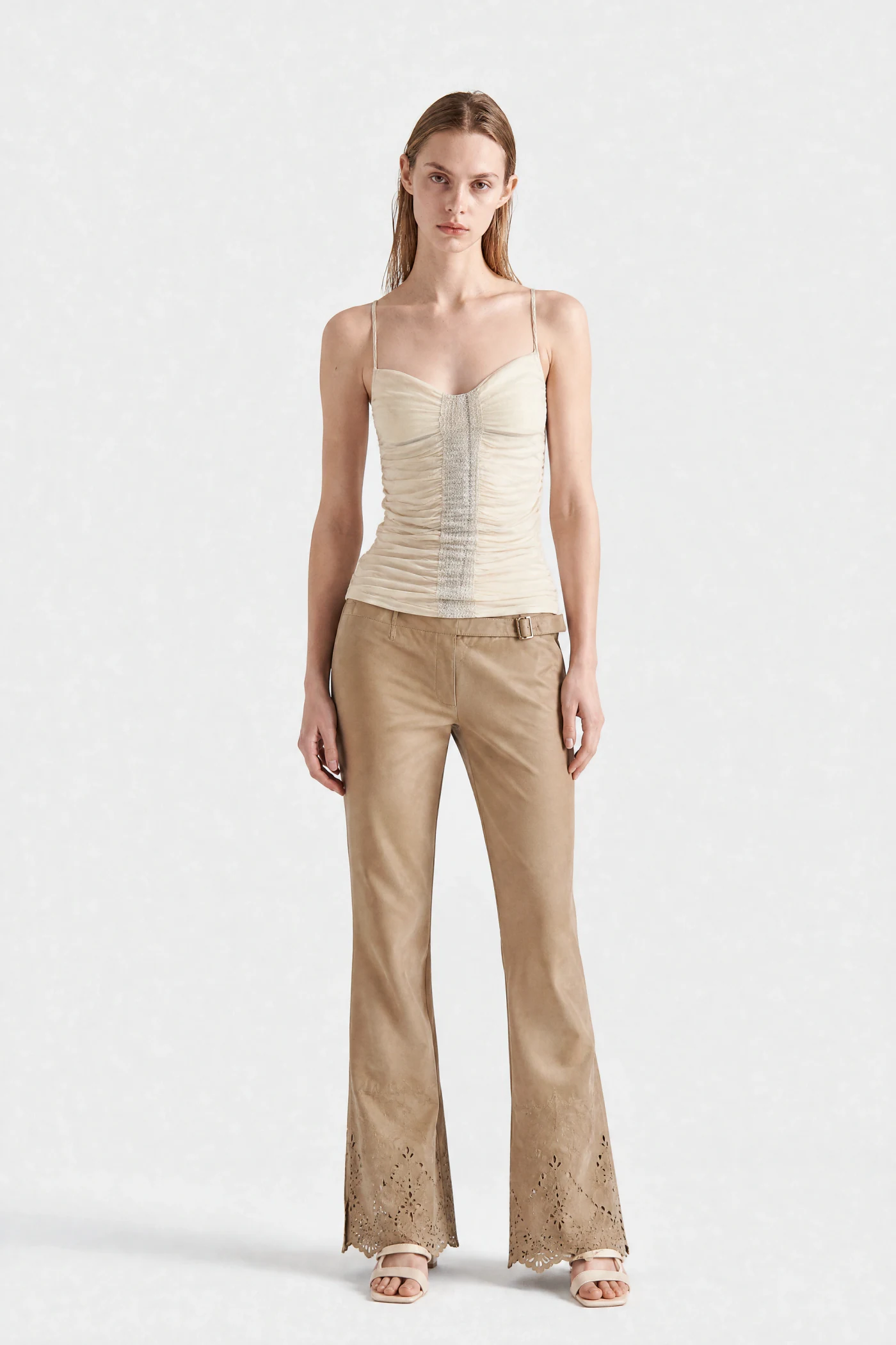 The same AI model in a ruched top and tan flared trousers, studio archive look