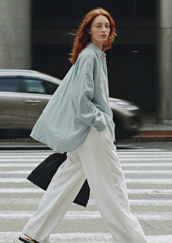 The same AI model crossing a city street in an oversized blue oxford shirt