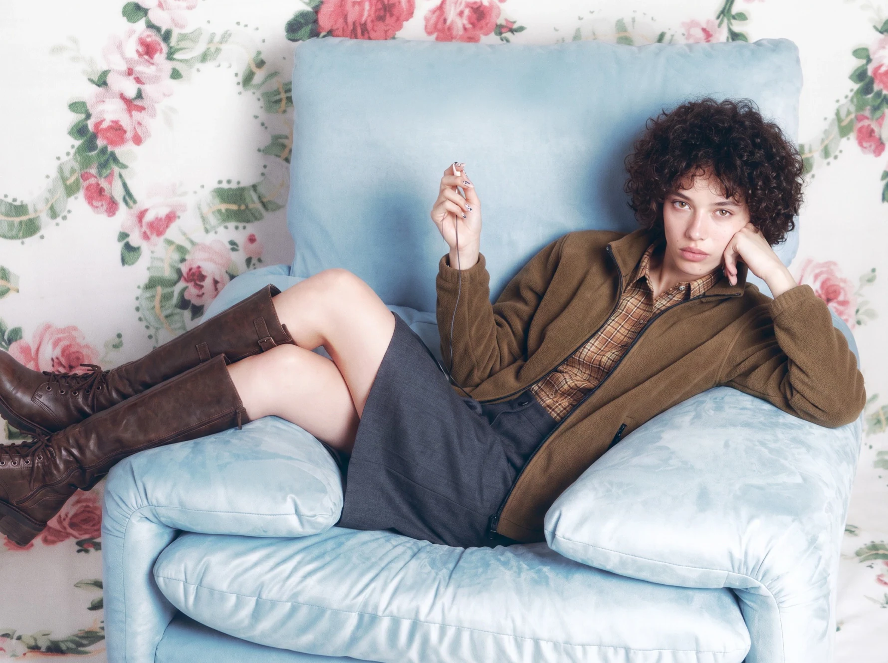 Campaign-ready creative generated before production: model in a powder-blue armchair against floral wallpaper