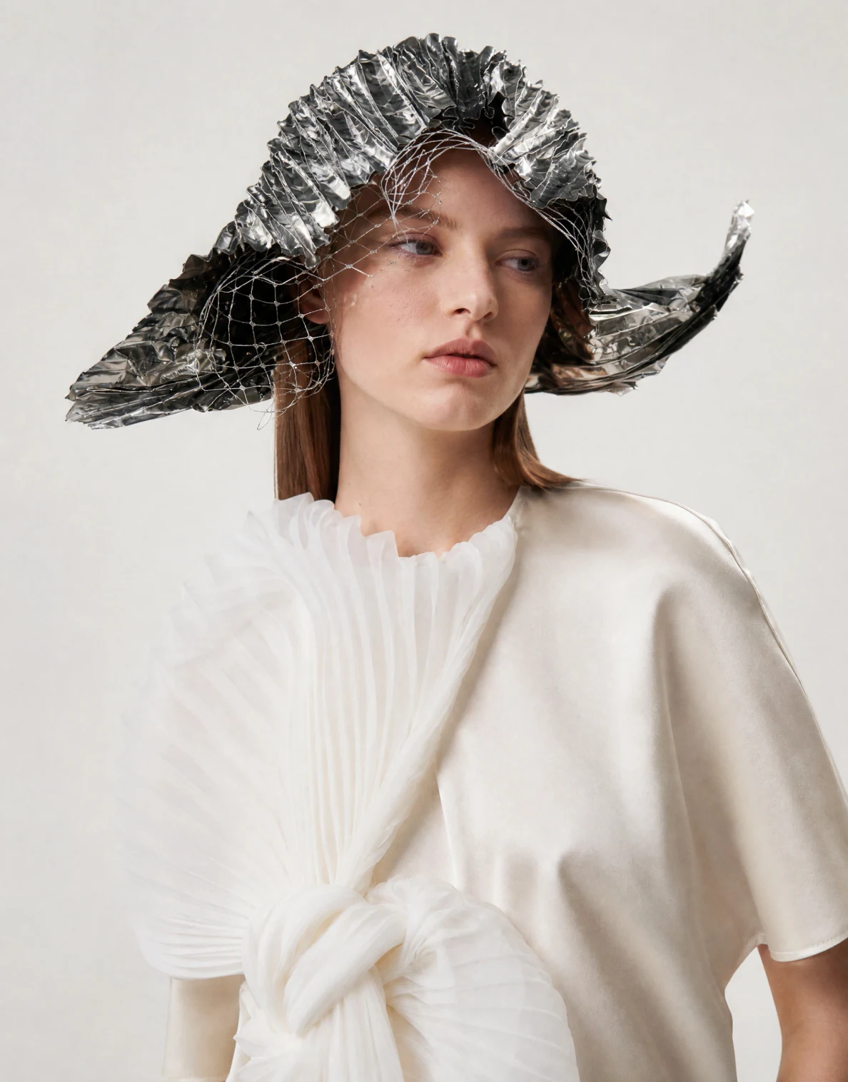 On-model photo generated from a flat lay: pleated white blouse styled with a sculptural silver hat