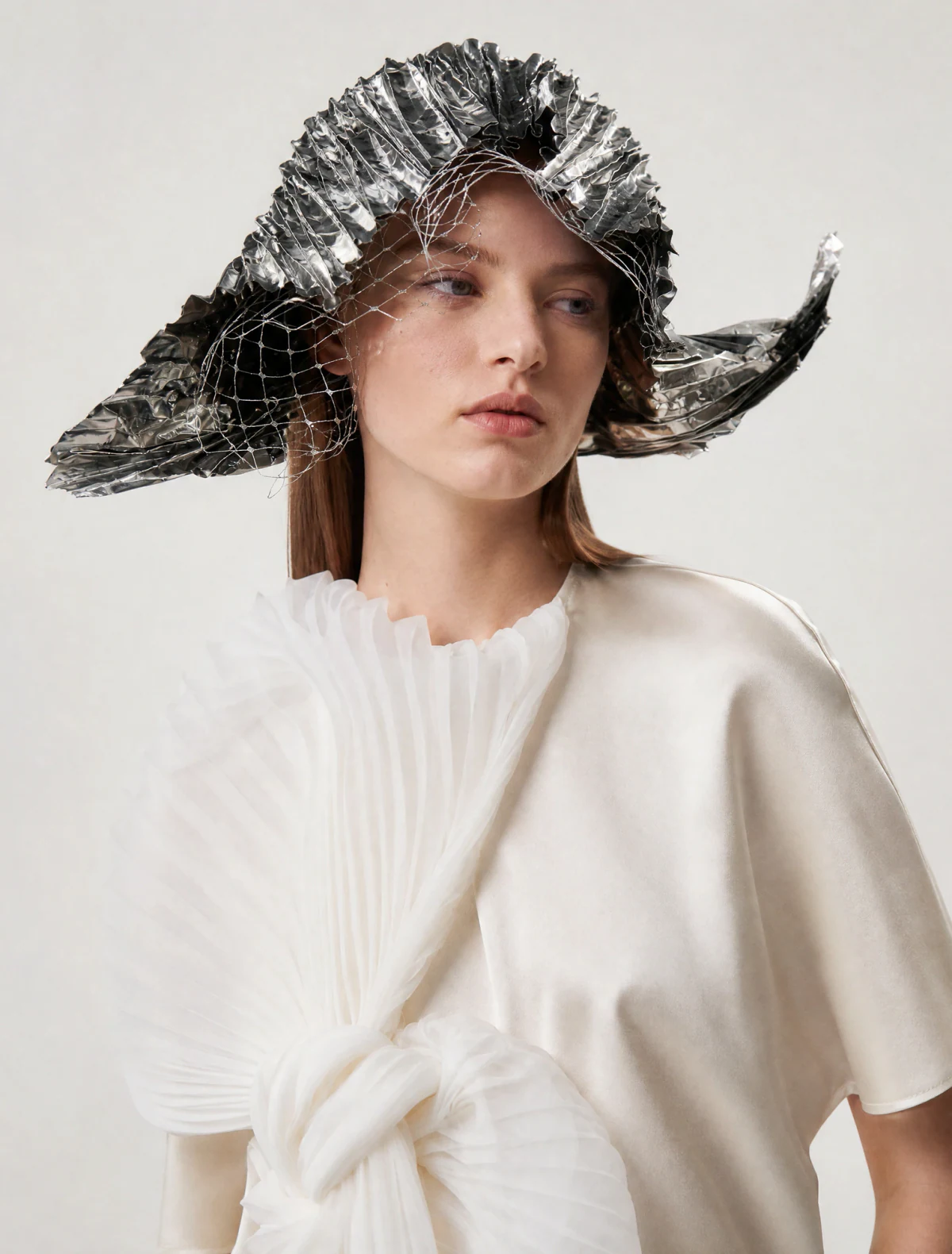 AI-generated on-model image: white pleated blouse with a sculptural foil hat, mid shot