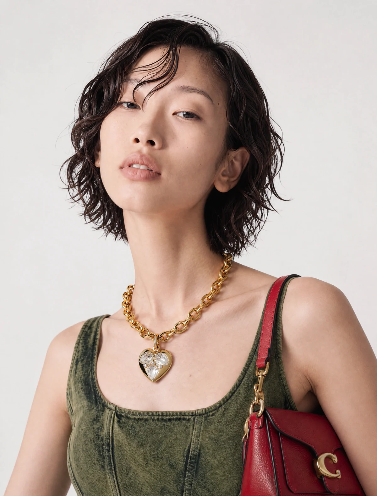 AI-generated on-model image: olive denim top with a chain necklace and a red charm bag, close-up portrait