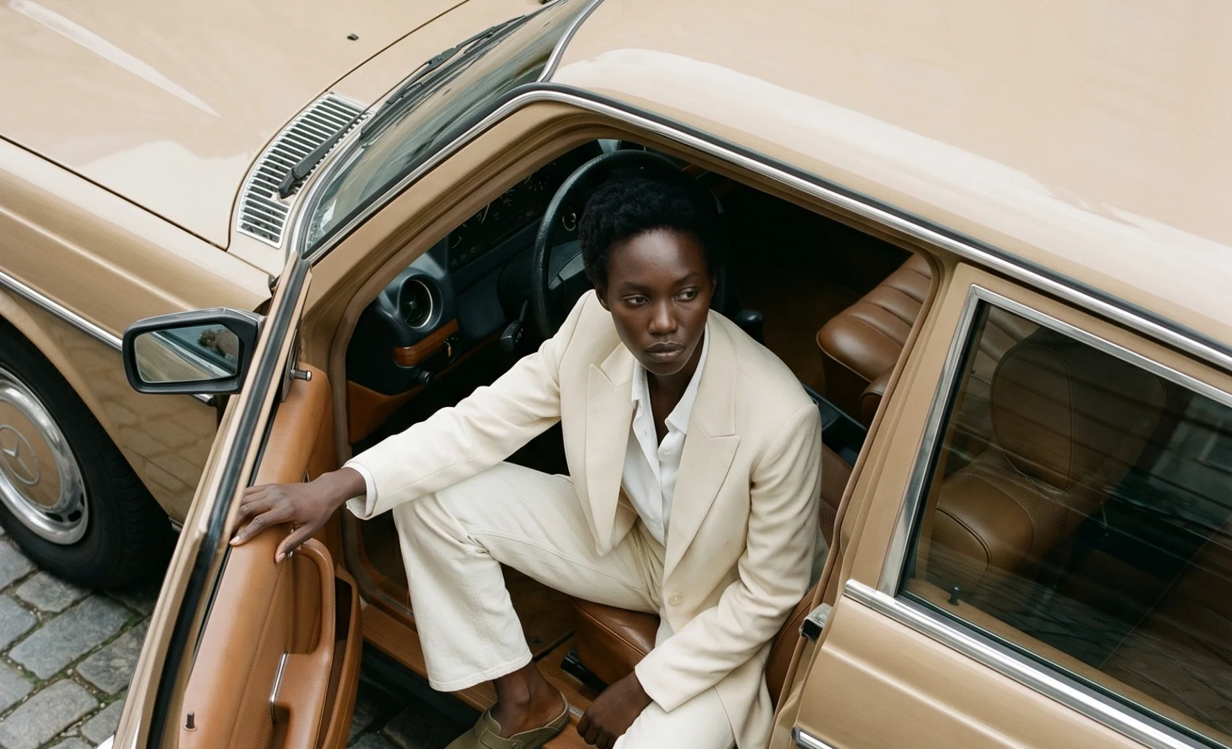 AI campaign imagery — model in a white suit stepping out of a vintage car