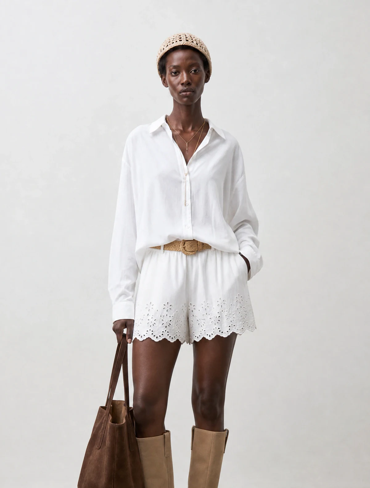 AI-generated on-model image: white linen shirt and shorts with a suede tote, mid shot on studio grey