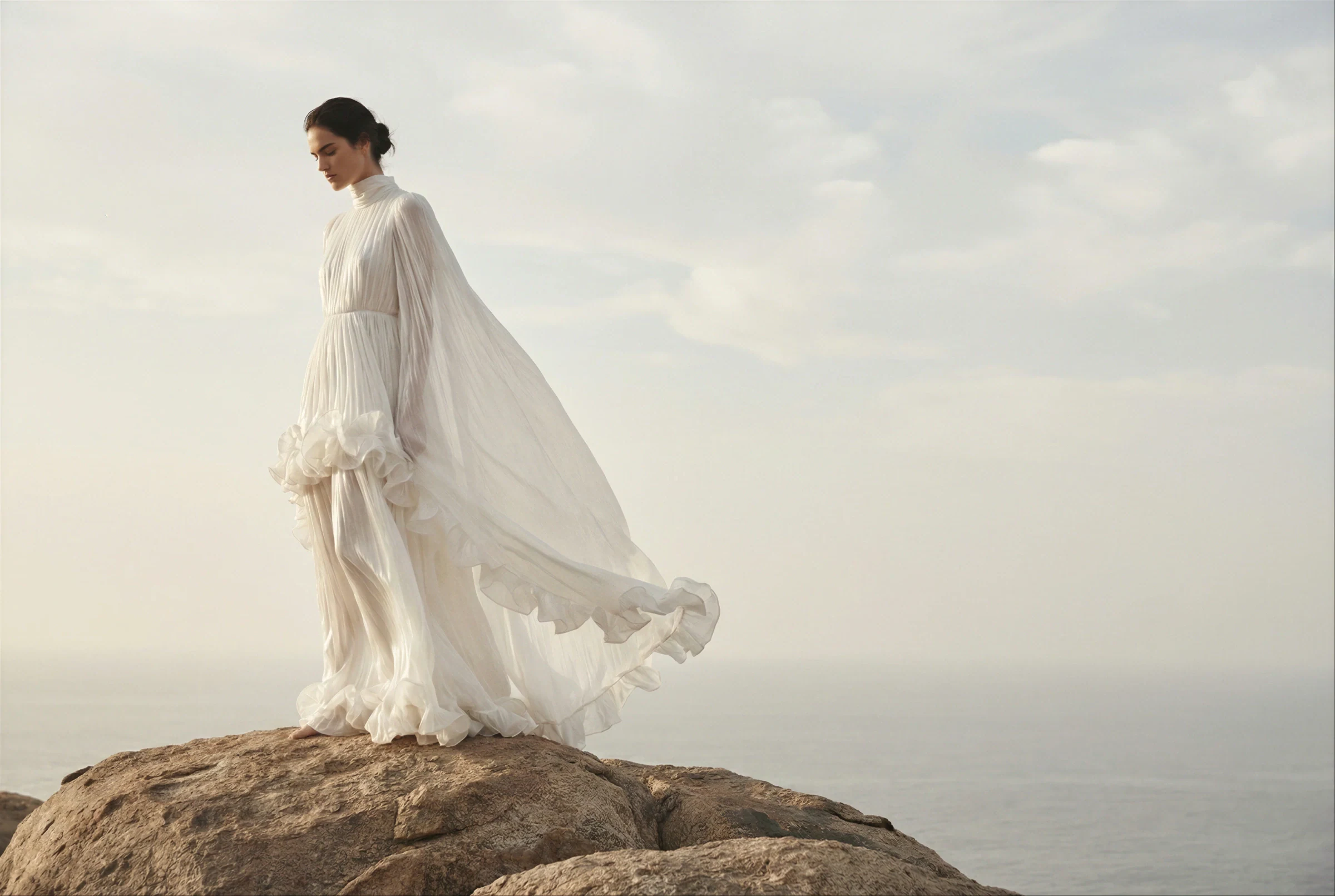 Campaign image generated before manufacturing: white gown photographed on a sea cliff